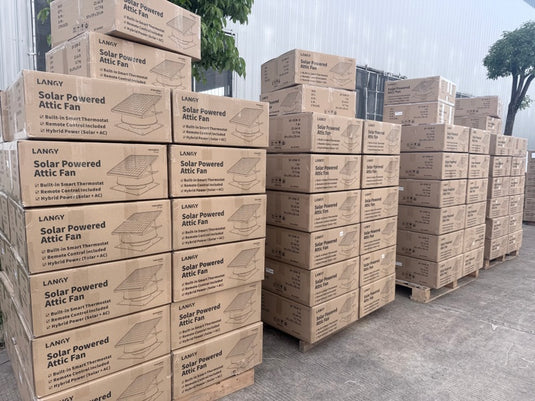 Stacks of cardboard boxes labeled 'Solar Powered Attic Fan' on pallets outdoors.